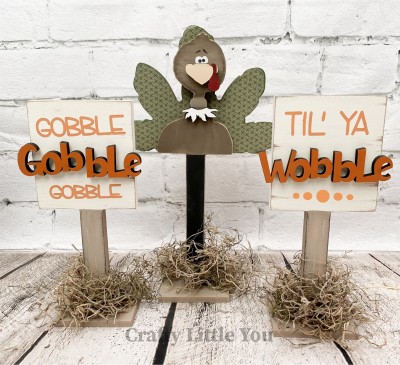 Unfinished kit measures apx. 11" tall on the turkey and includes wooden MDF: 
* 1 turkey feathers on stand
* 1 turkey body, beak, and neck feather overlay
* 2 square signs on stands
* 1 "Gobble" wood word
* 1 "Wobble" wood word
* 3 bases
* Vinyl stencils
* Vinyl eyes and eyebrows