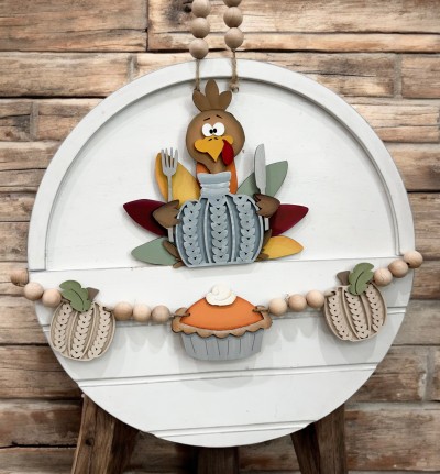 Unfinished kit is sized to fit the Front Door Circle and includes wooden MDF:
*1 set of turkey feathers
*1 turkey body overlay
*1 beak and eyes overlay
*1 turkey hand with attached fork
*1 turkey hand with attached knife
*1 turtleneck sweater overlay
*2 sweater pumpkins with front overlays
*2 leaves
*1 pumpkin pie with crust and whipped cream overlay
*2 pieces Velcro